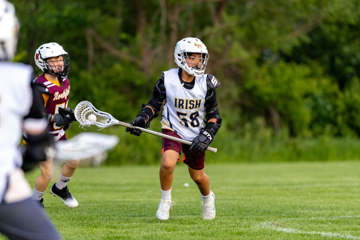 Youth lacrosse player tries to fake out his defender and look for a pass to a teammate