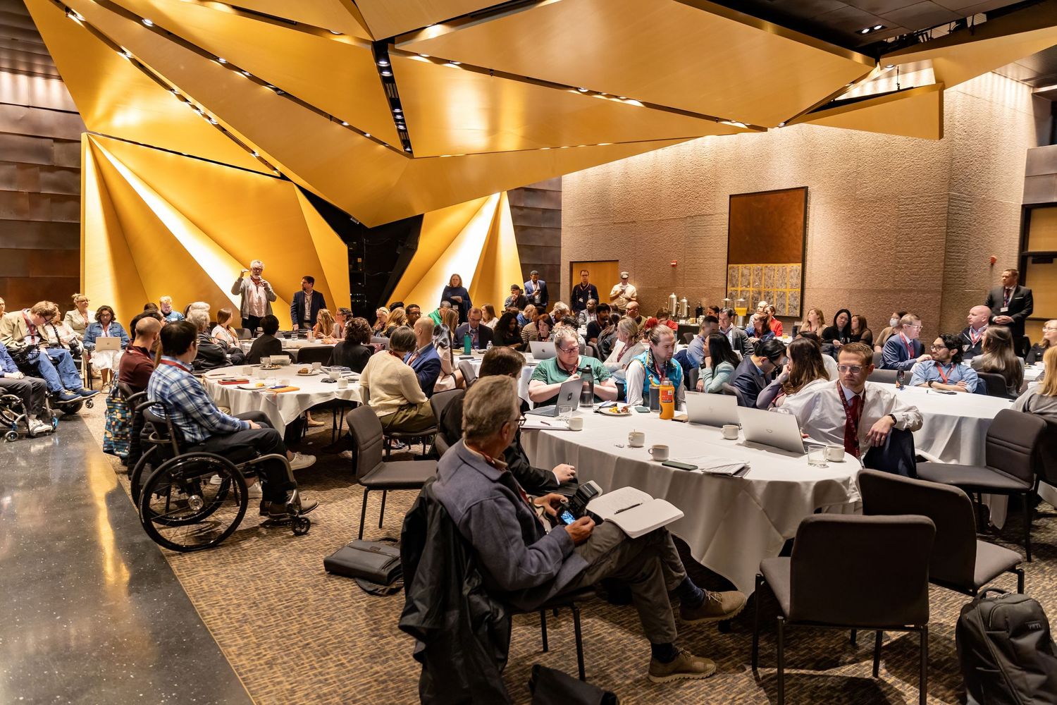 Groups of tables of attendees at the Design of Medical Device Conference at University of Minnesota listen to corporate sponsor presentation