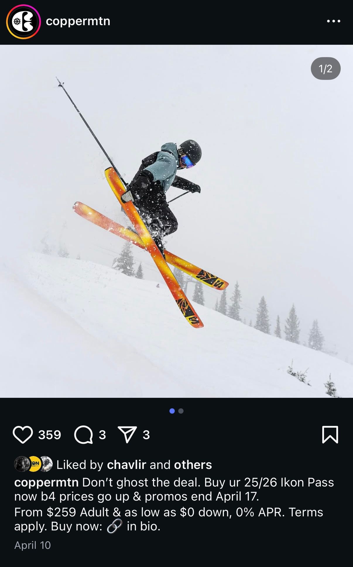 A skier performs an aerial trick off a snowy jump in a winter mountain setting with trees visible in the background.