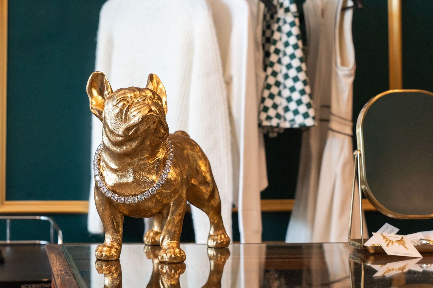 Gold French Bulldog figurine with diamond necklace on glass counter in luxury fashion boutique.
