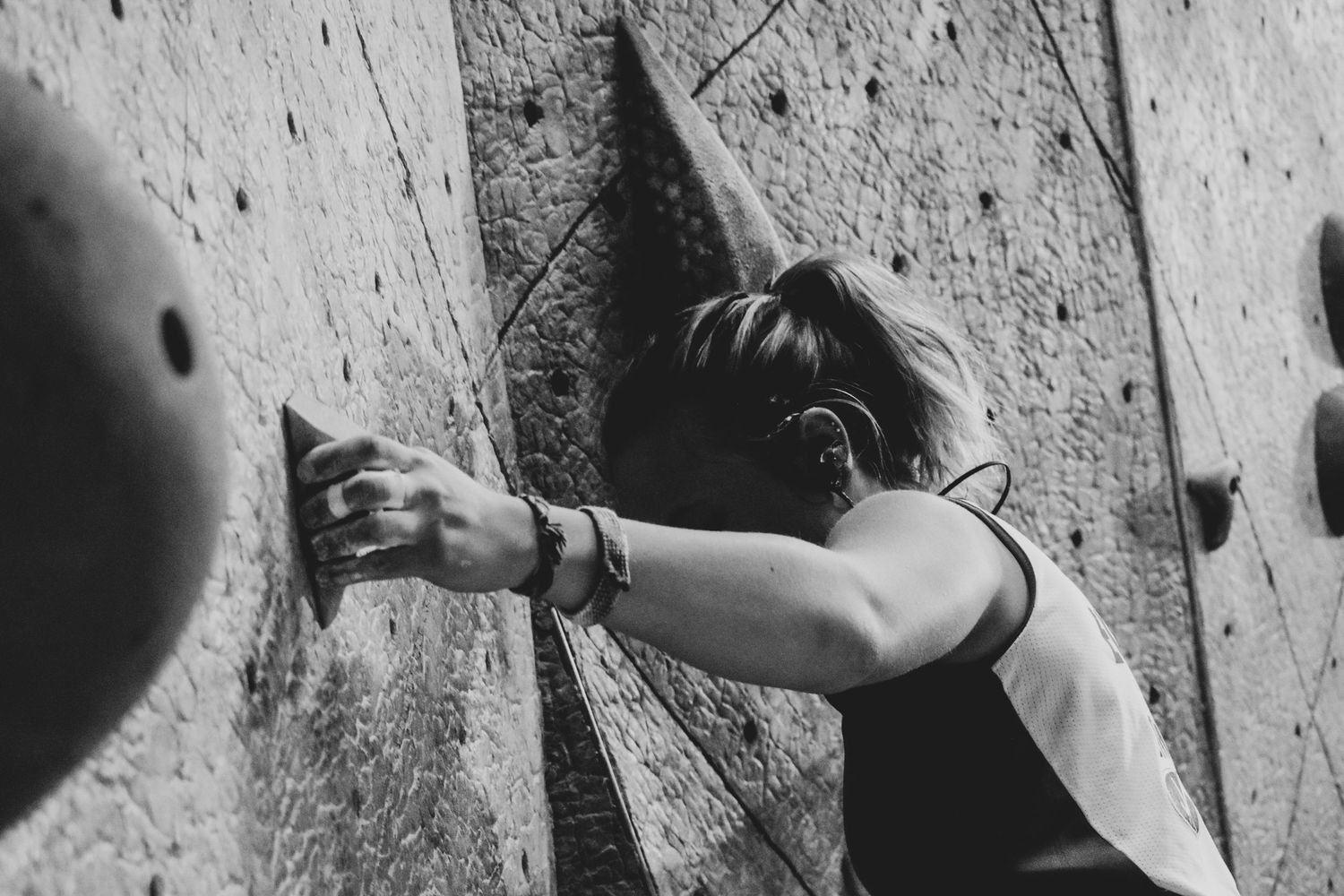 Climber reaching for a distant hold on an indoor climbing wall, shot in black and white.