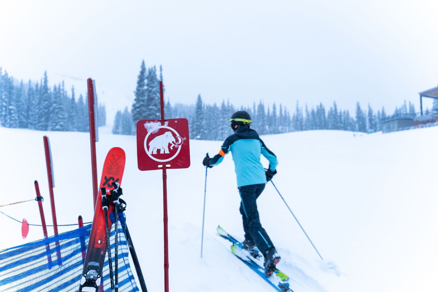 Skier navigating past a red and white trail marker sign on a snow-covered mountain slope.