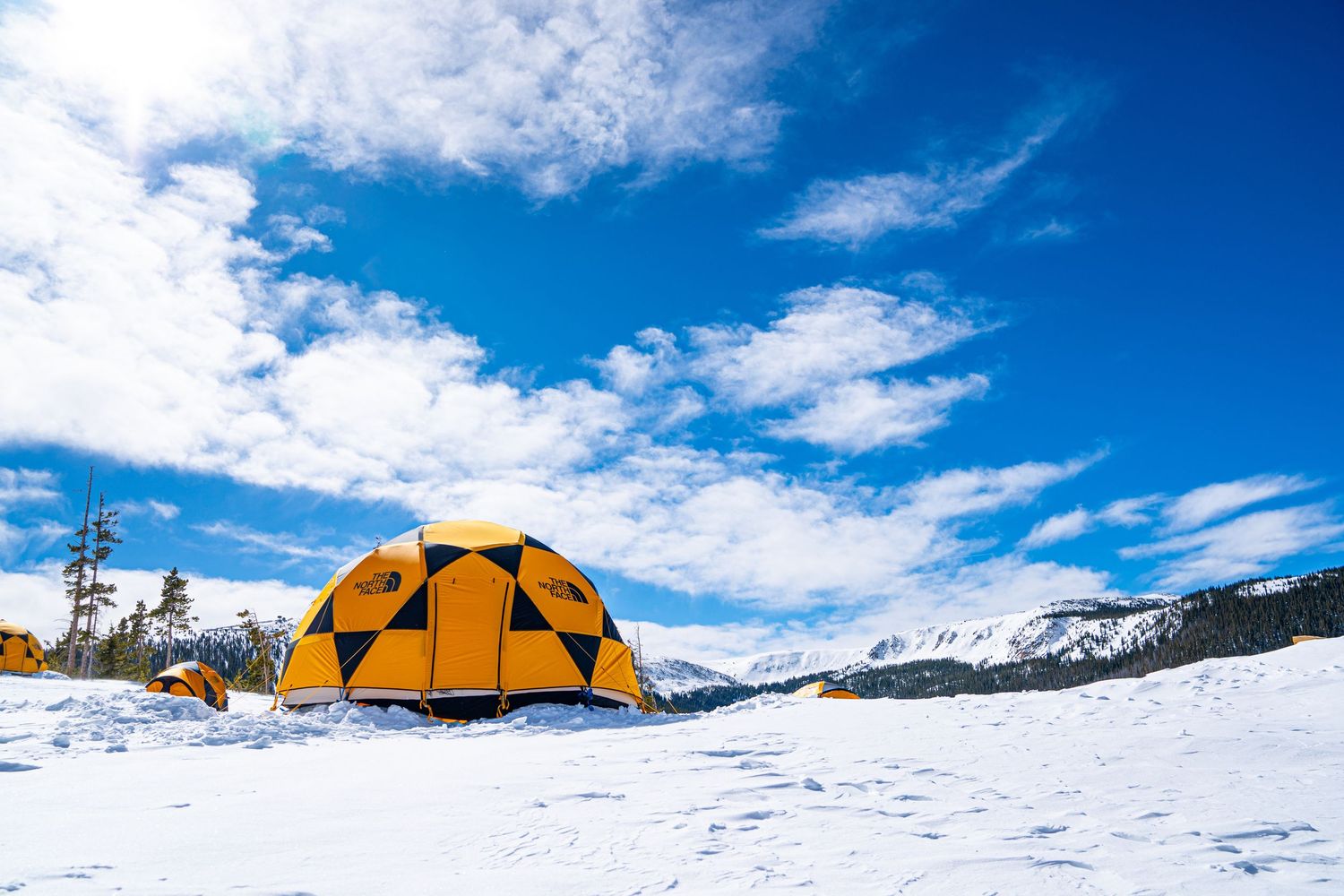 Yellow dome tent against bright blue winter sky with snow-covered mountains.
