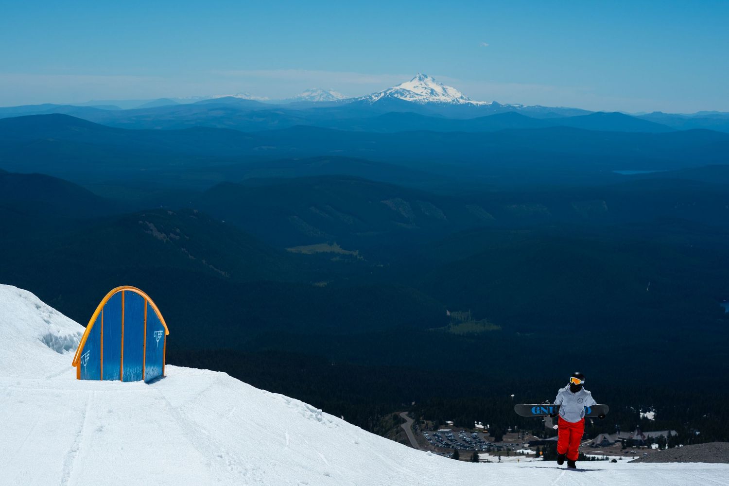 Snow-covered terrain park with blue rail feature and mountain vista in background.