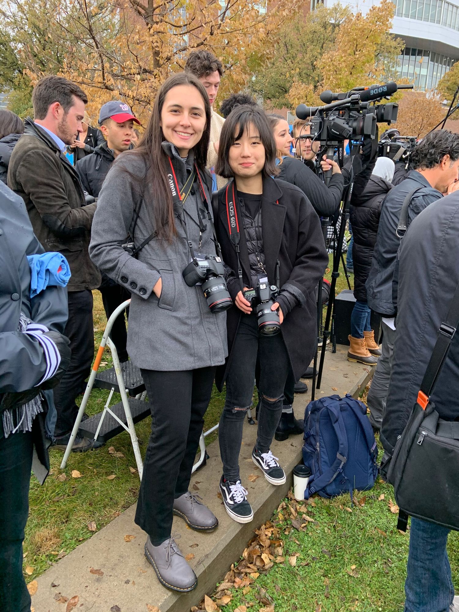 A group of photographers and spectators gathered outdoors with camera equipment during an autumn day.