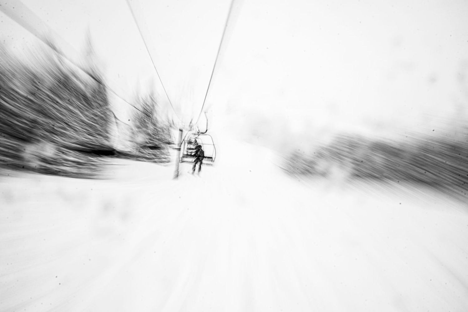 Blurred motion shot of a ski lift chair against a snowy white background creating an artistic abstract effect.