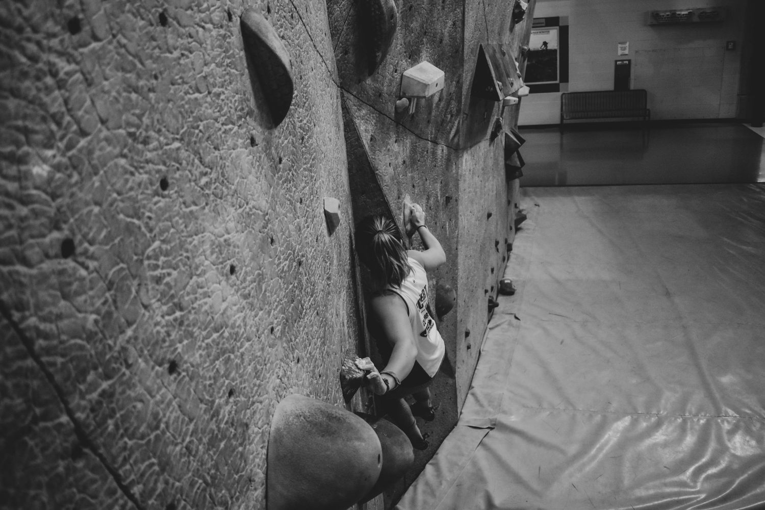 Indoor rock climber scaling a challenging climbing wall while gripping textured holds in black and white.