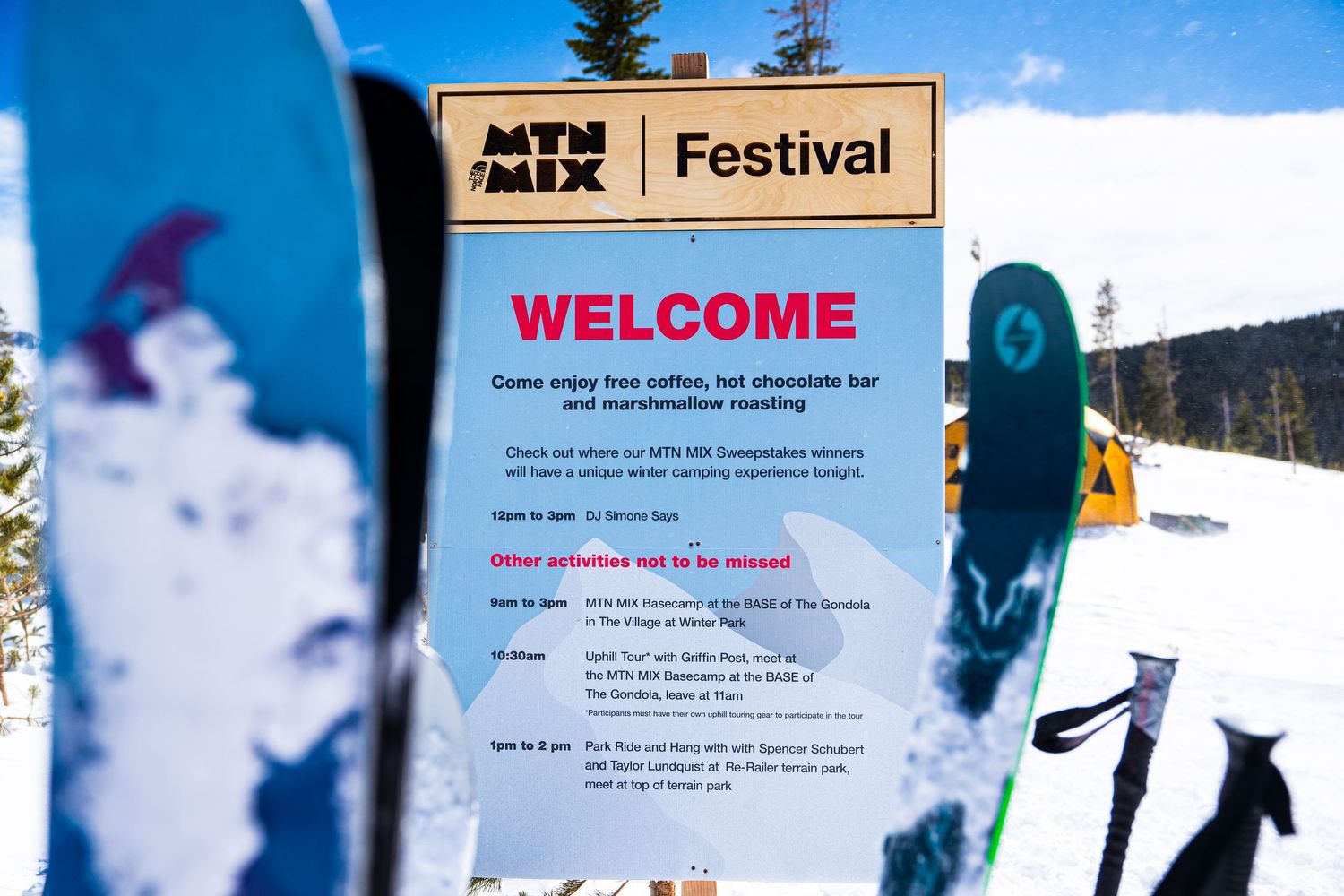 Festival welcome sign framed by skis with snowy mountain landscape in background.