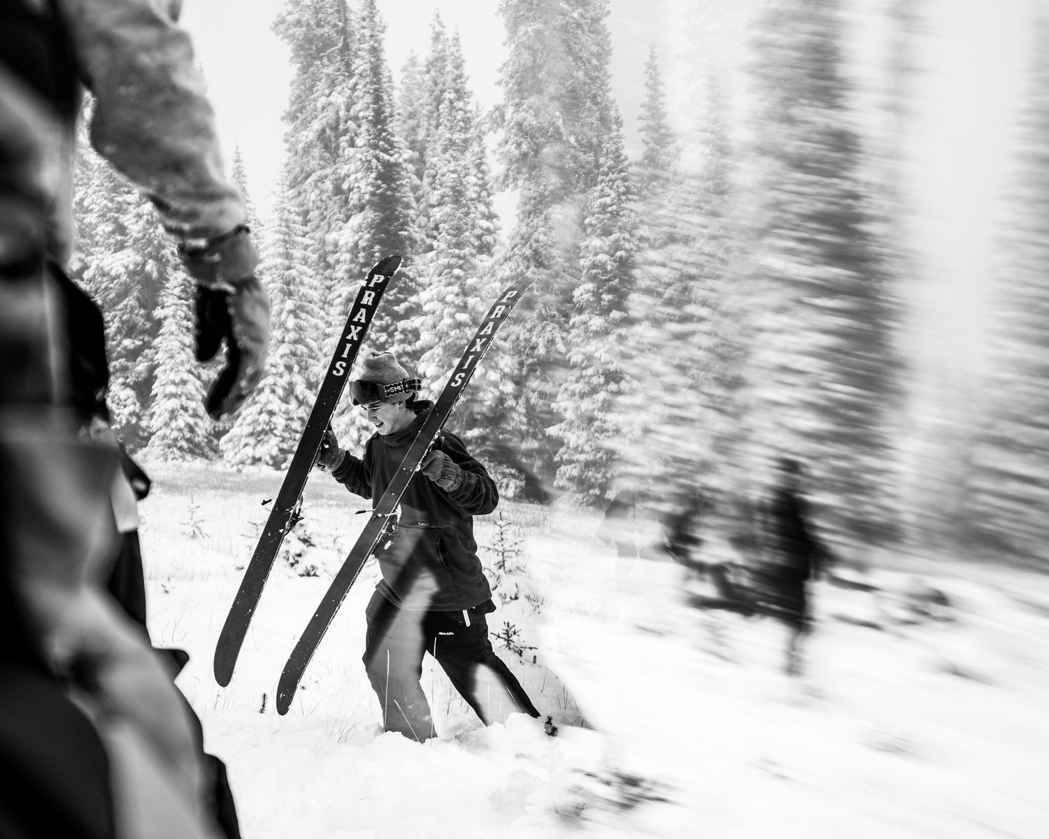 Black and white action shot of skiers hiking through deep powder snow in forest.