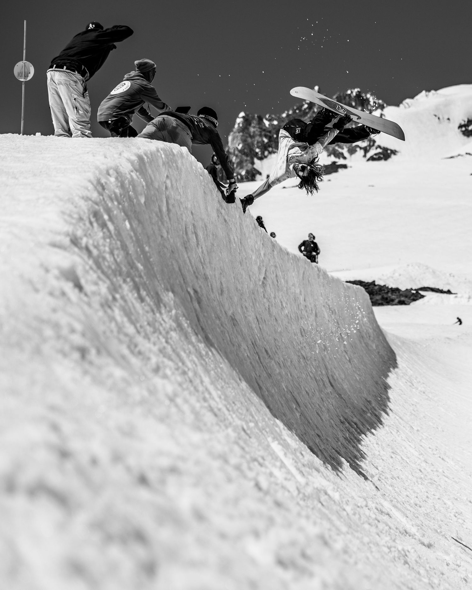 Black and white photo of snowboarders dropping into a steep powder bowl.