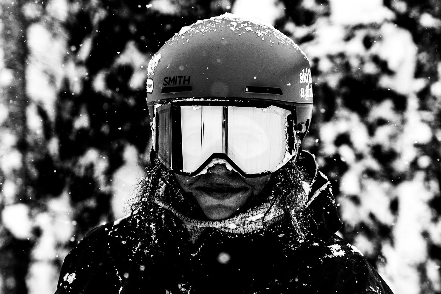 Close-up black and white shot of ski helmet and goggles covered in snow.