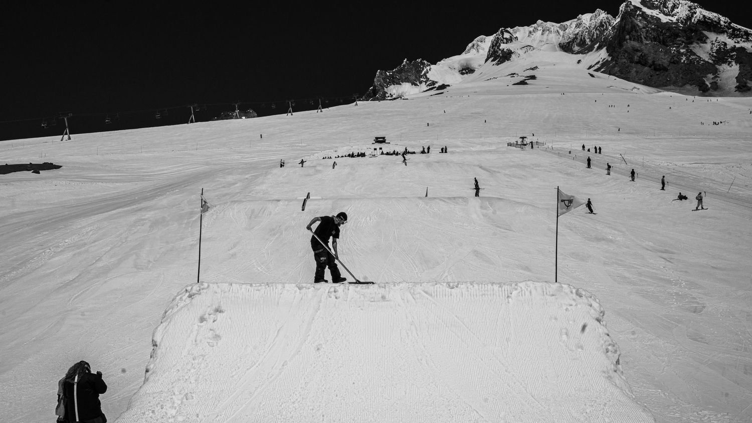 Black and white aerial view of a skier on a snowy terrain park jump.