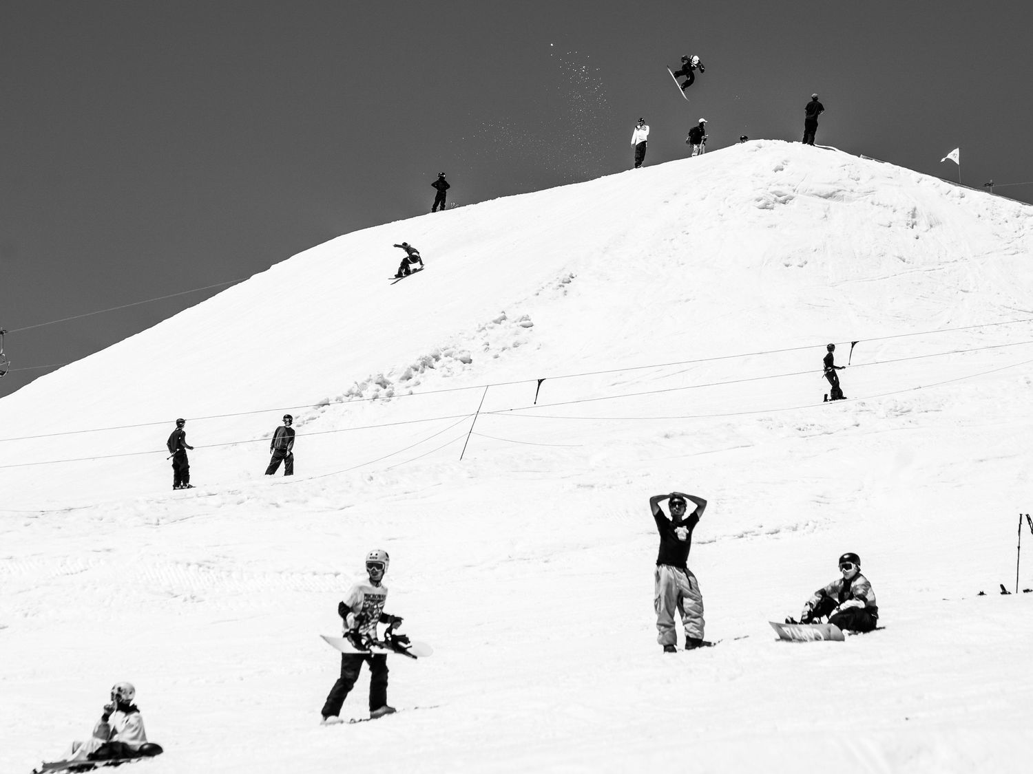 Black and white shot of skiers and snowboarders scattered across a snowy hill slope.