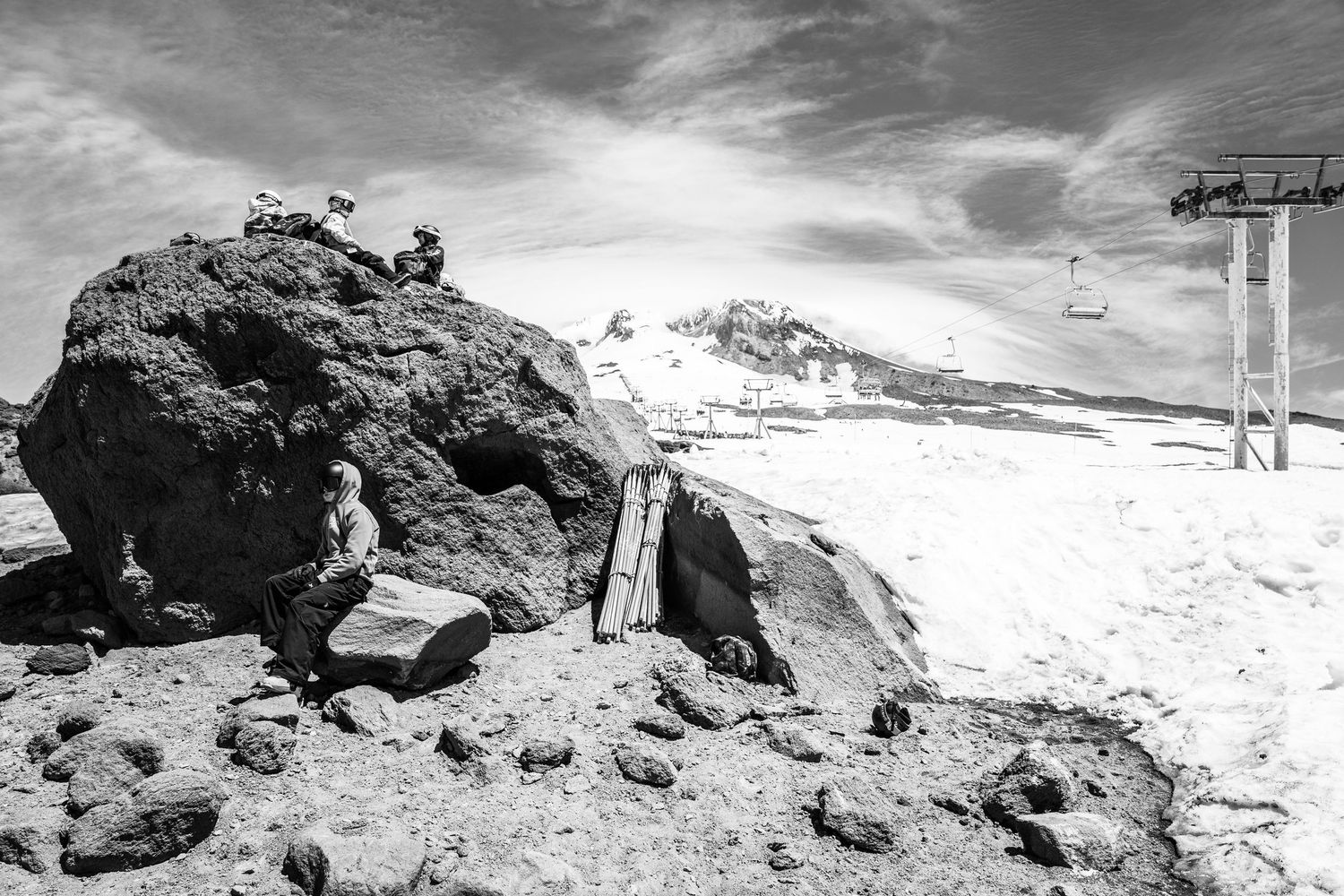 A black and white photograph of rocky terrain with snow and ski lift equipment in the background.