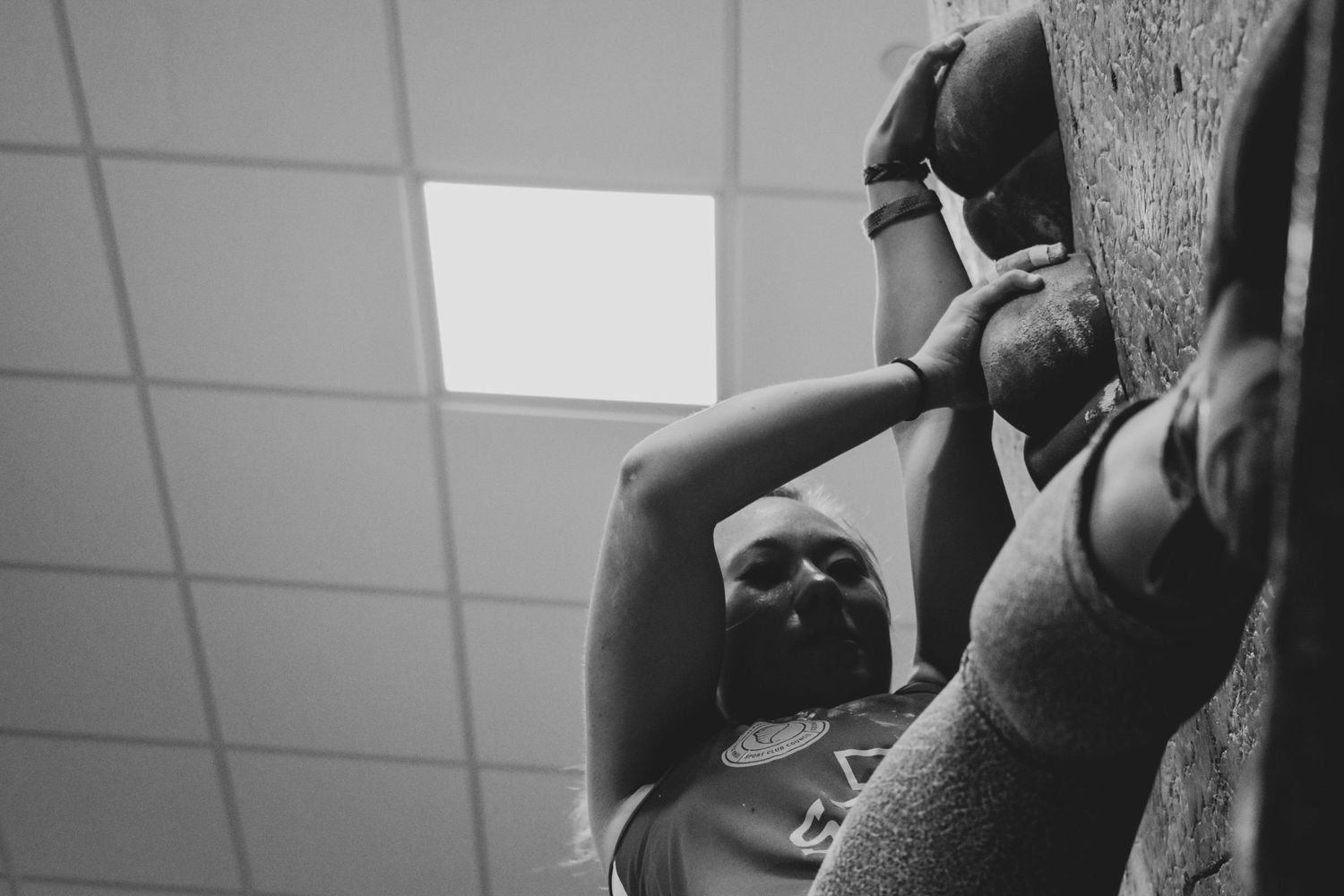 Low angle view of climber ascending an indoor climbing wall beneath fluorescent lighting.