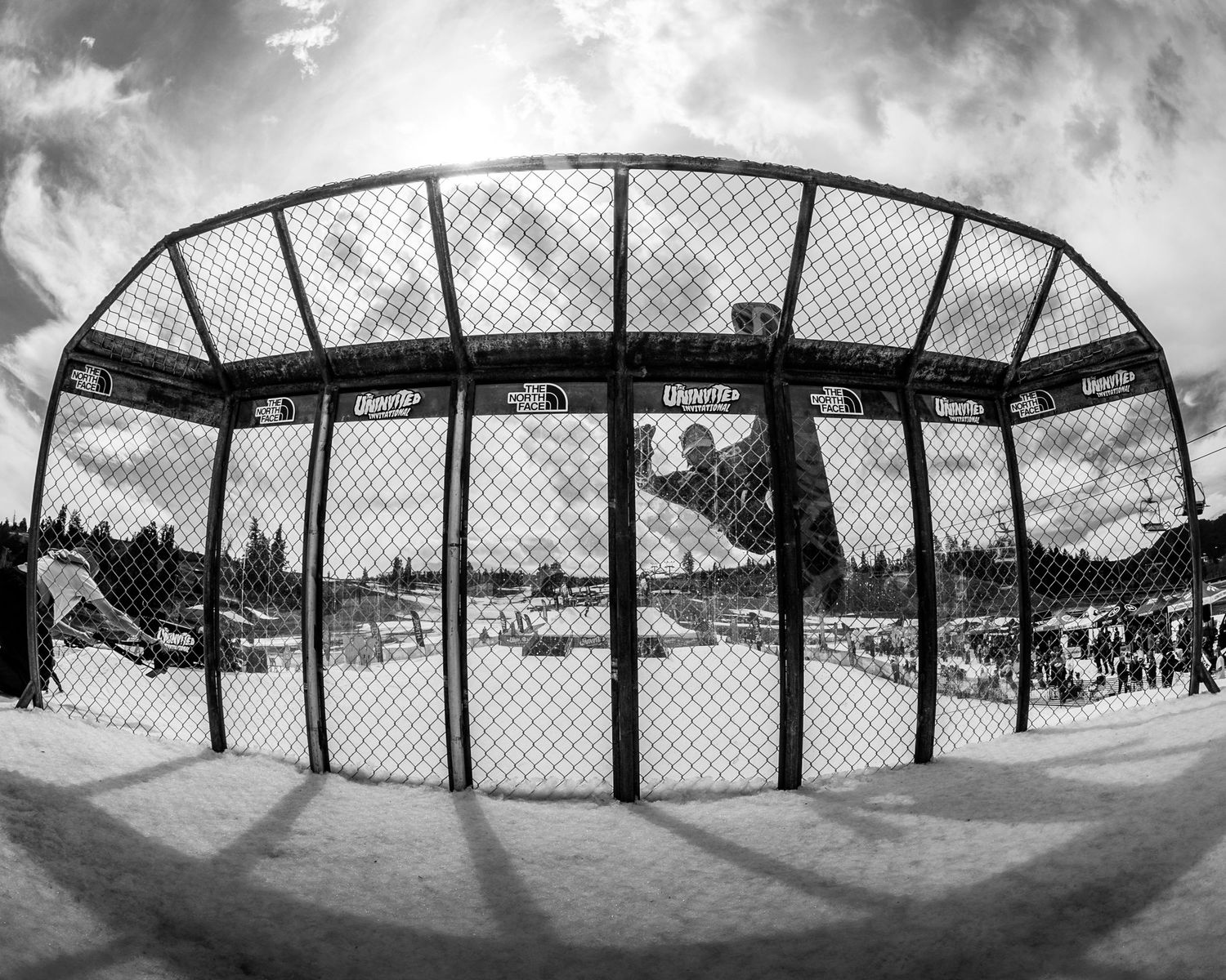 Black and white fisheye photo of a skate cage structure at a snowy winter resort.