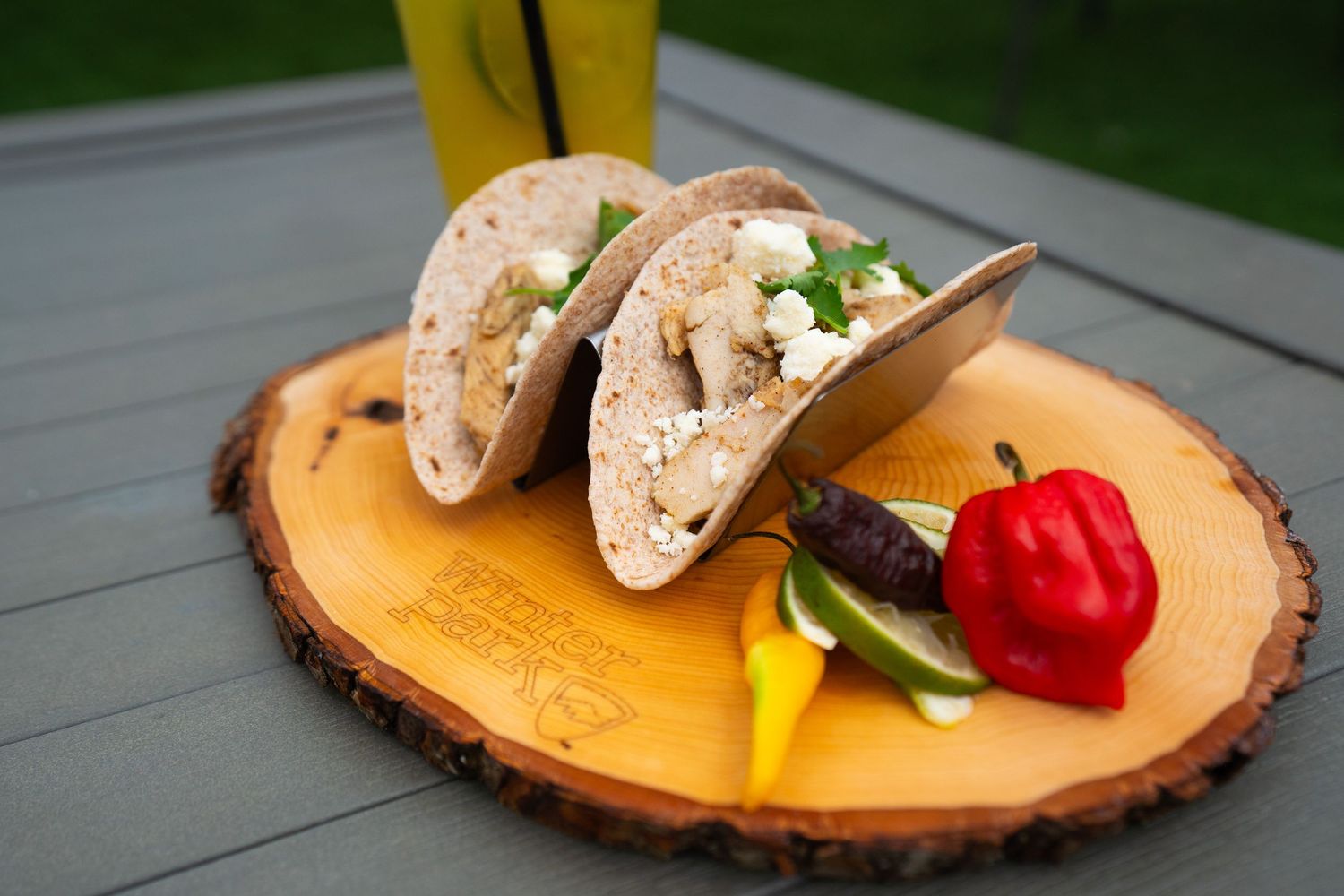 Two fish tacos served on a wooden platter with colorful pepper garnish.