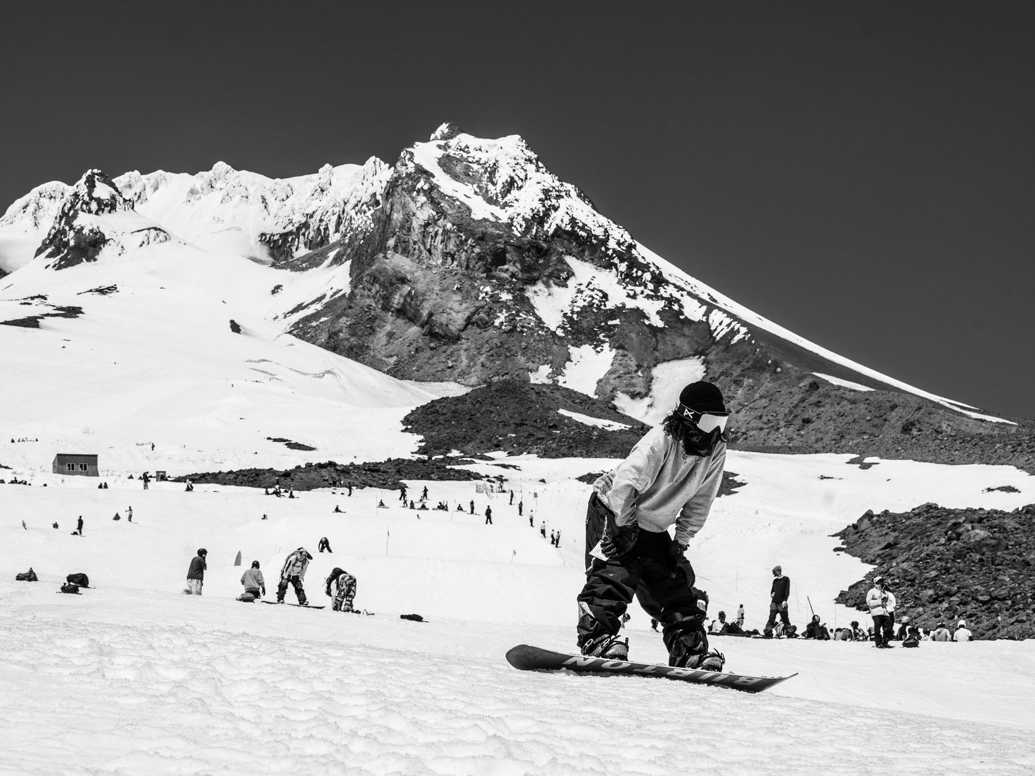 Snowboarder rides down Mt Hood with majestic snow-covered peak in the background.