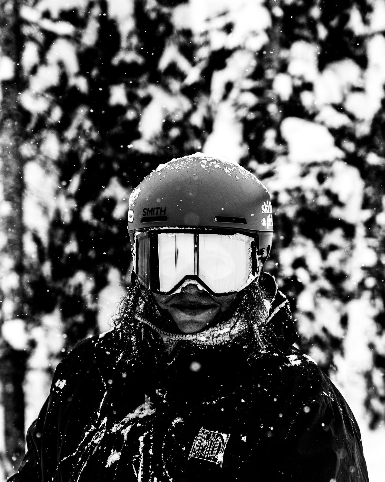 Winter sports enthusiast in black gear with snow-covered helmet against snowy forest.