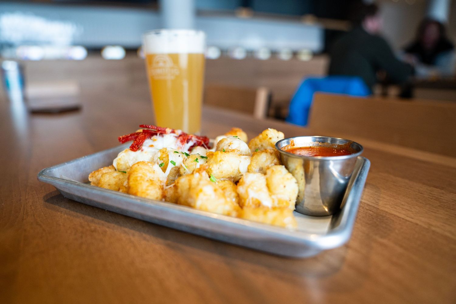 Crispy tater tots with cheese sauce and a beer on a metal serving tray.