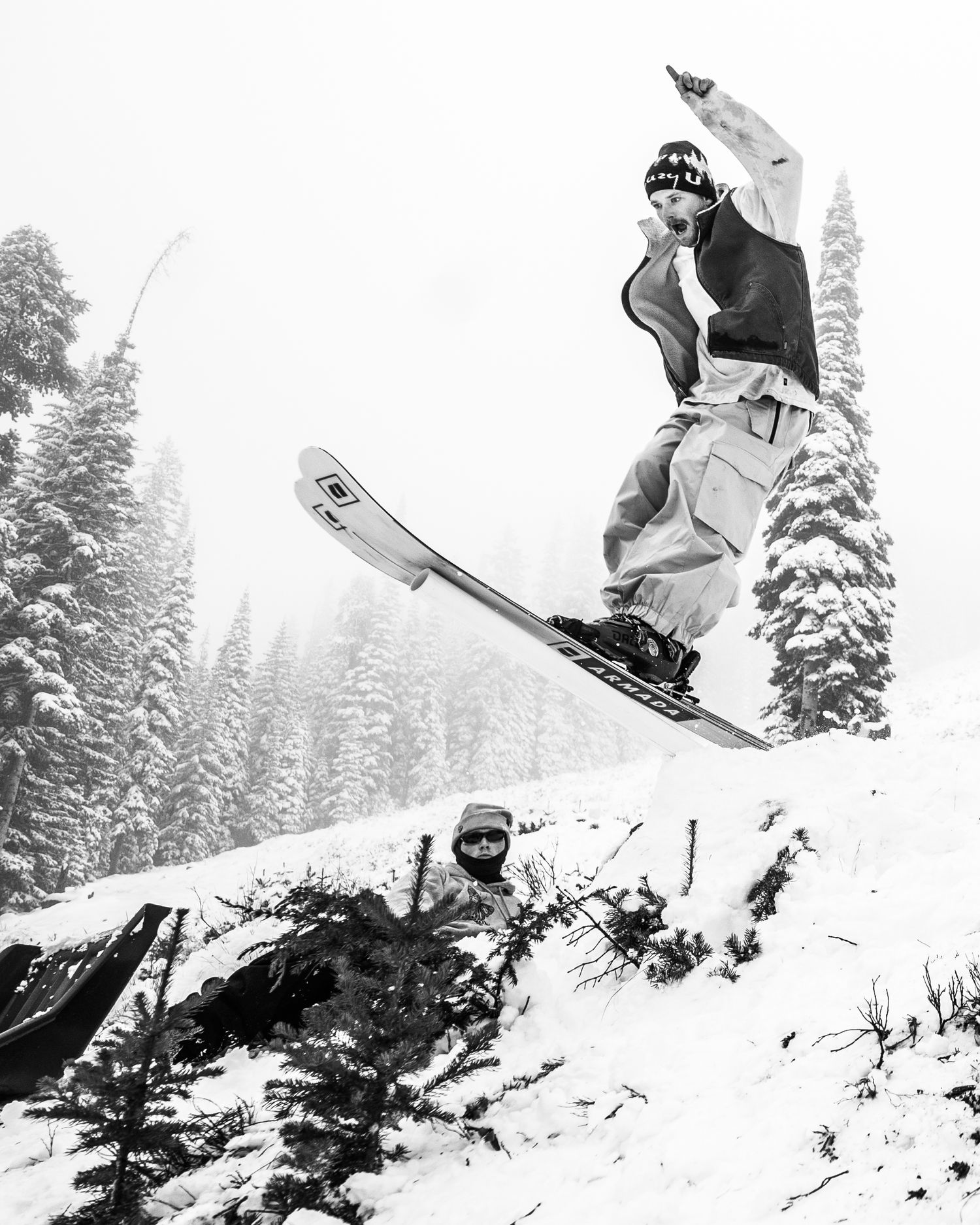 Vintage black and white photo of a skier catching air off a snowy jump in a winter forest landscape.