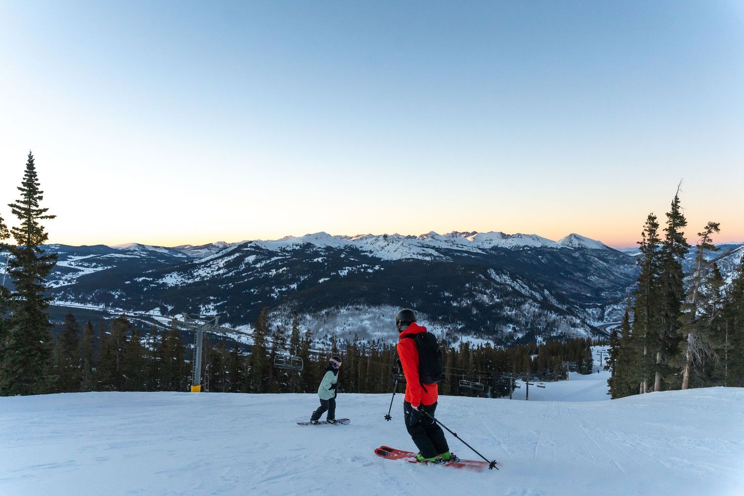 Skiers descending snowy slope with panoramic mountain valley views.