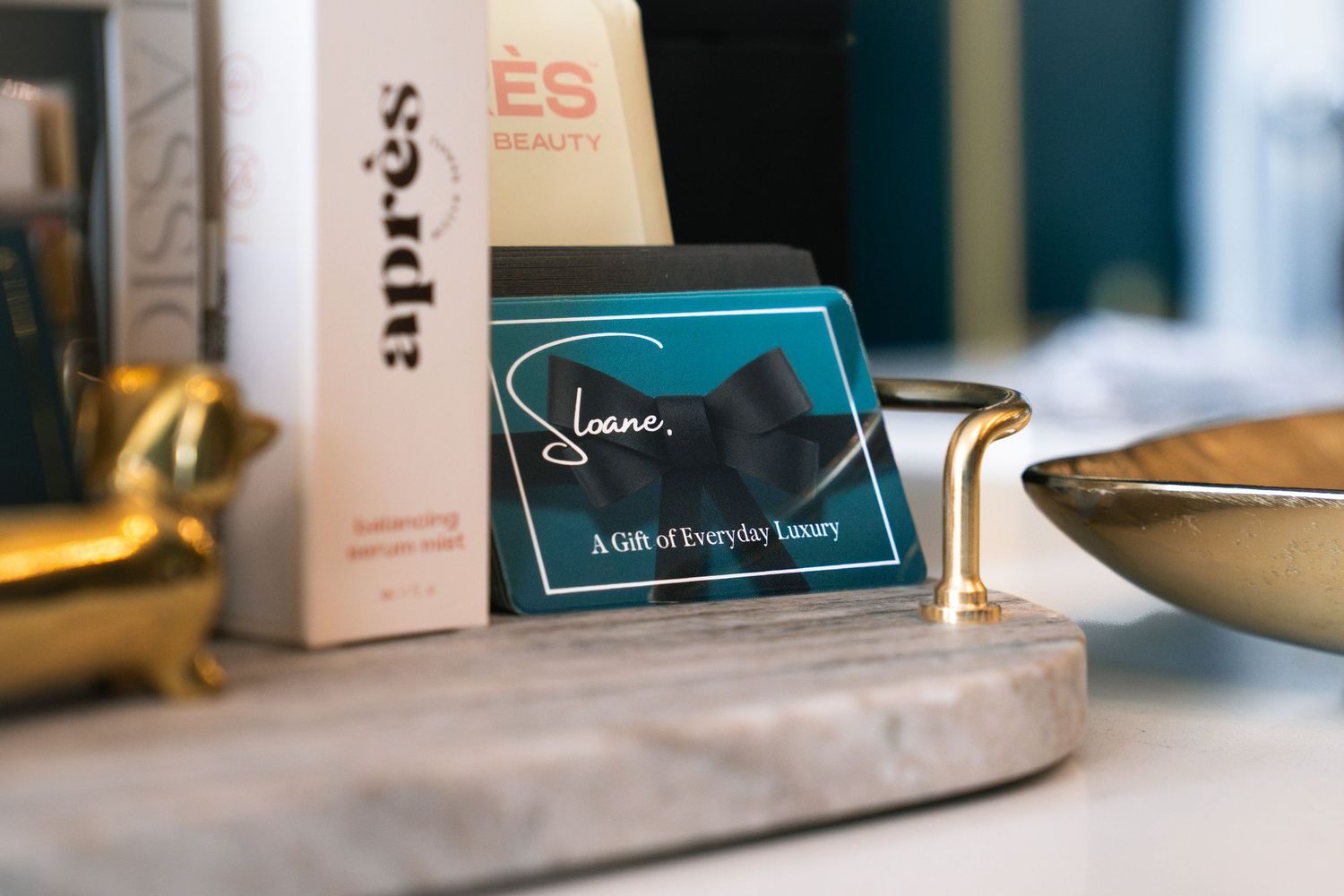 Sloane gift card displayed on marble tray with Apres beauty products and gold accessories.