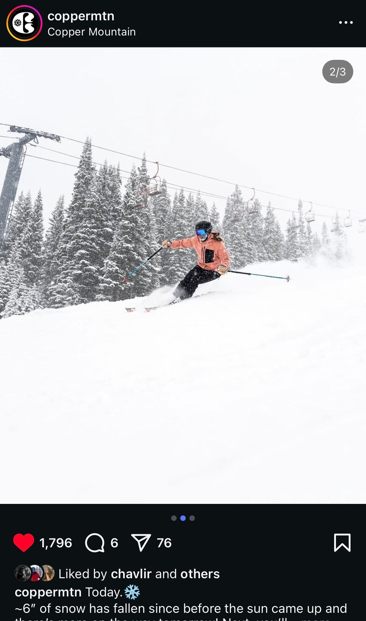 A skier carves through fresh powder snow on a snowy mountain slope with evergreen trees and ski lifts in the background.
