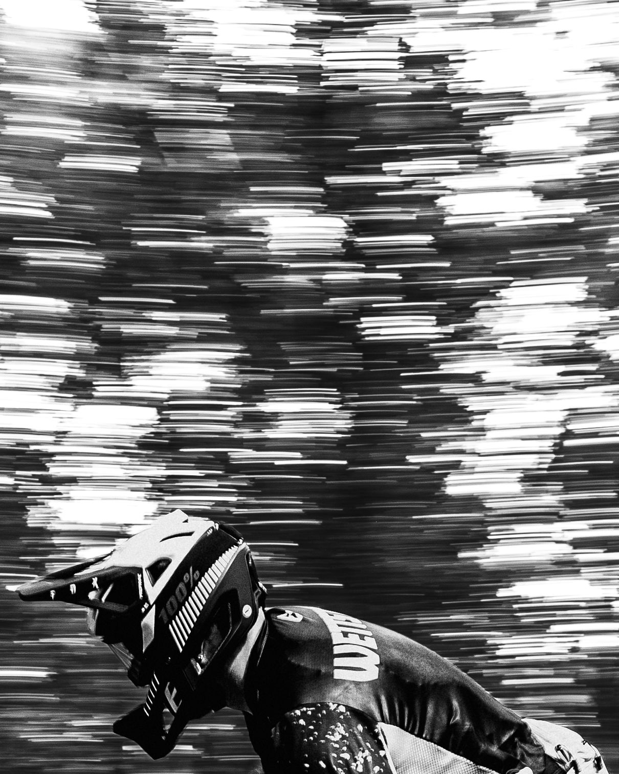 Black and white motion blur photograph of a person riding a racing bicycle on a cycling track.
