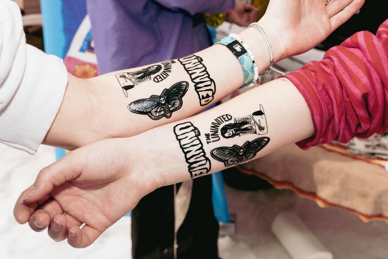 Two arms side by side displaying matching black temporary tattoos with butterfly designs on their wrists.