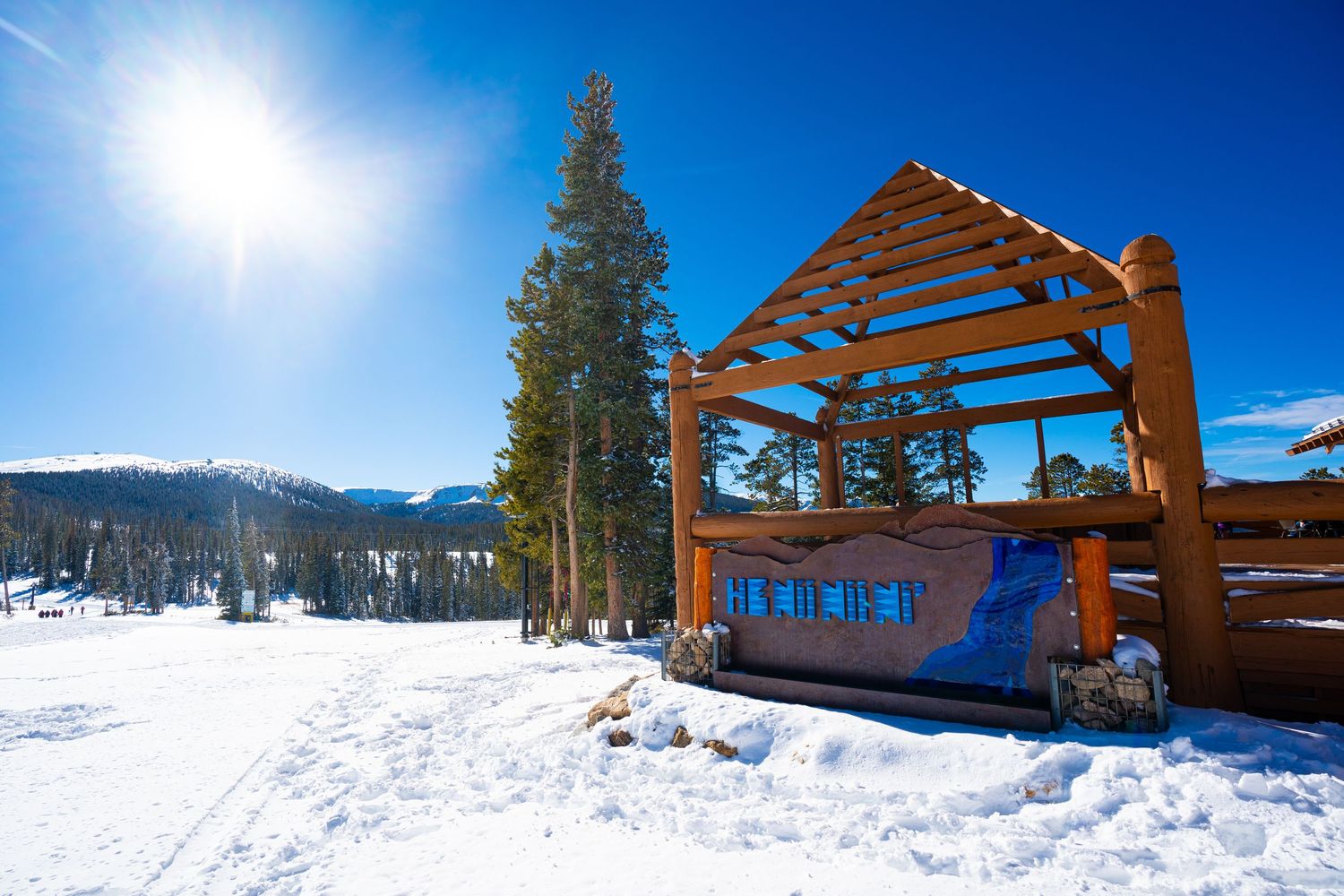 Wooden ski shelter structure on snowy mountain slope with bright sun overhead.