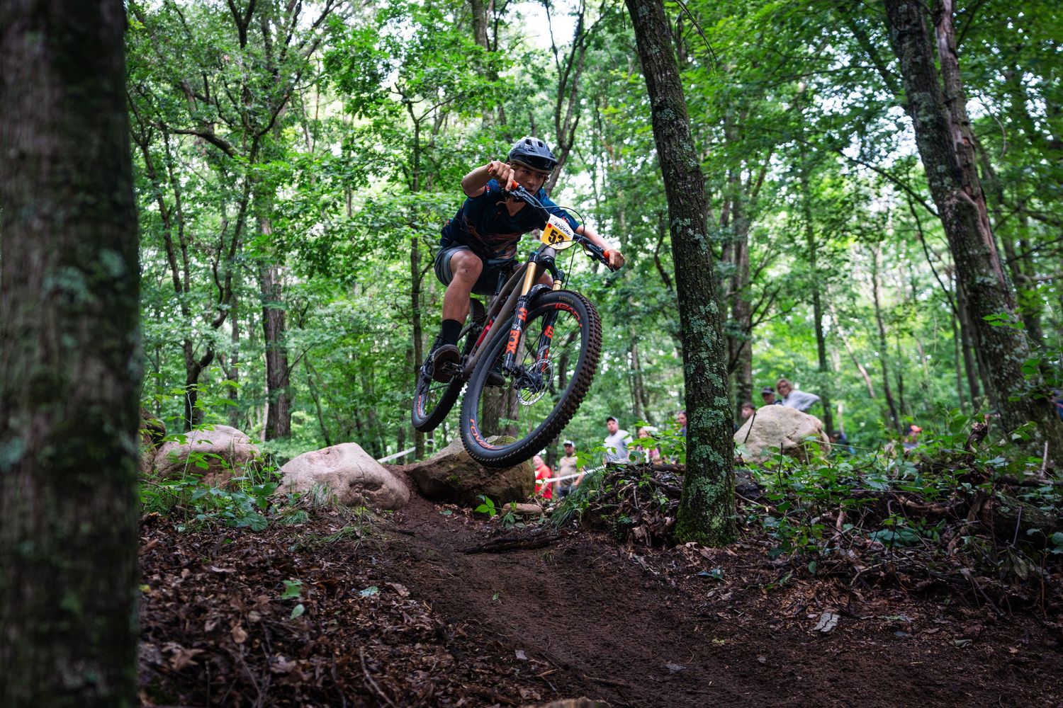 Mountain biker navigates a steep dirt trail through a densely forested area during a summer ride.