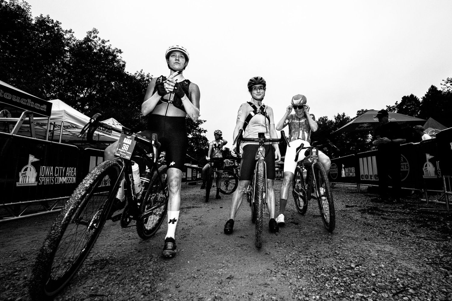 Black and white photo of cyclists in helmets walking bikes at an outdoor mountain biking event.