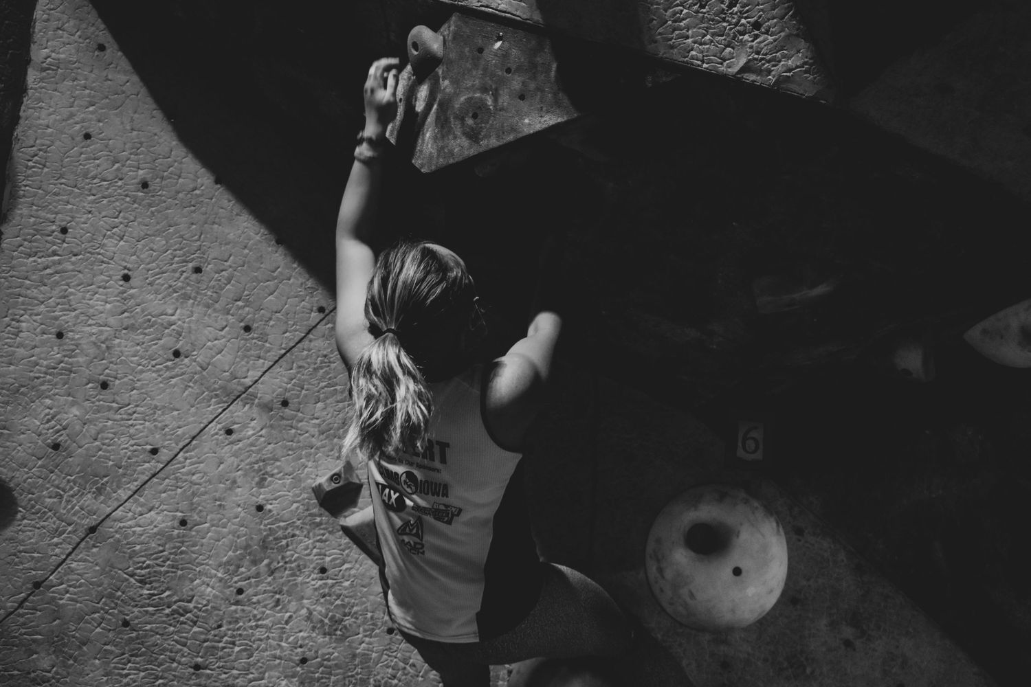 Indoor rock climber ascending wall shown from below in monochrome photography.