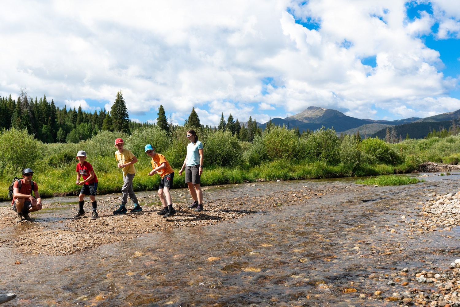 Group exploring rocky mountain stream bed with mountains and forest in background.