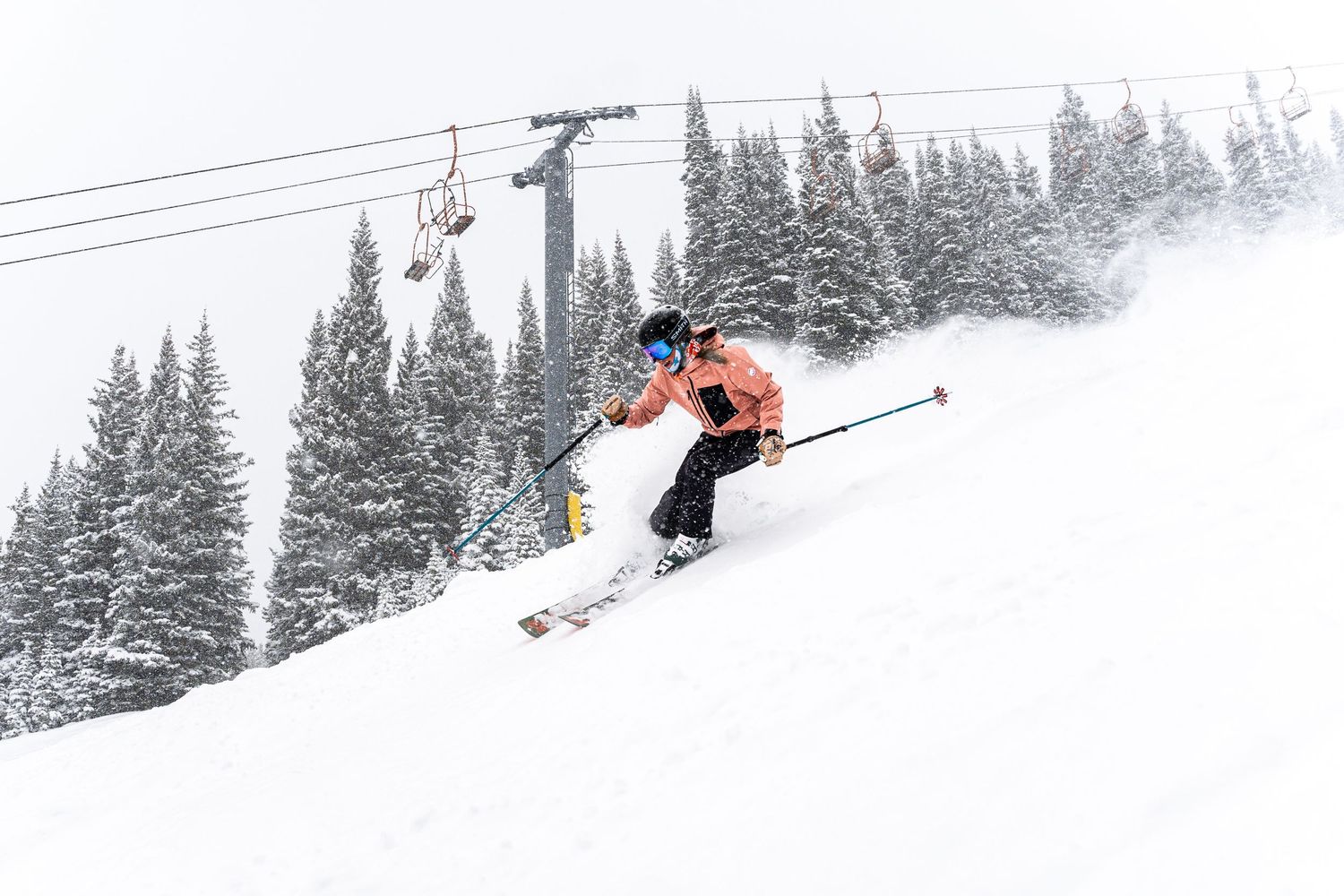 Skier carving down a steep slope with ski lift cables visible overhead.