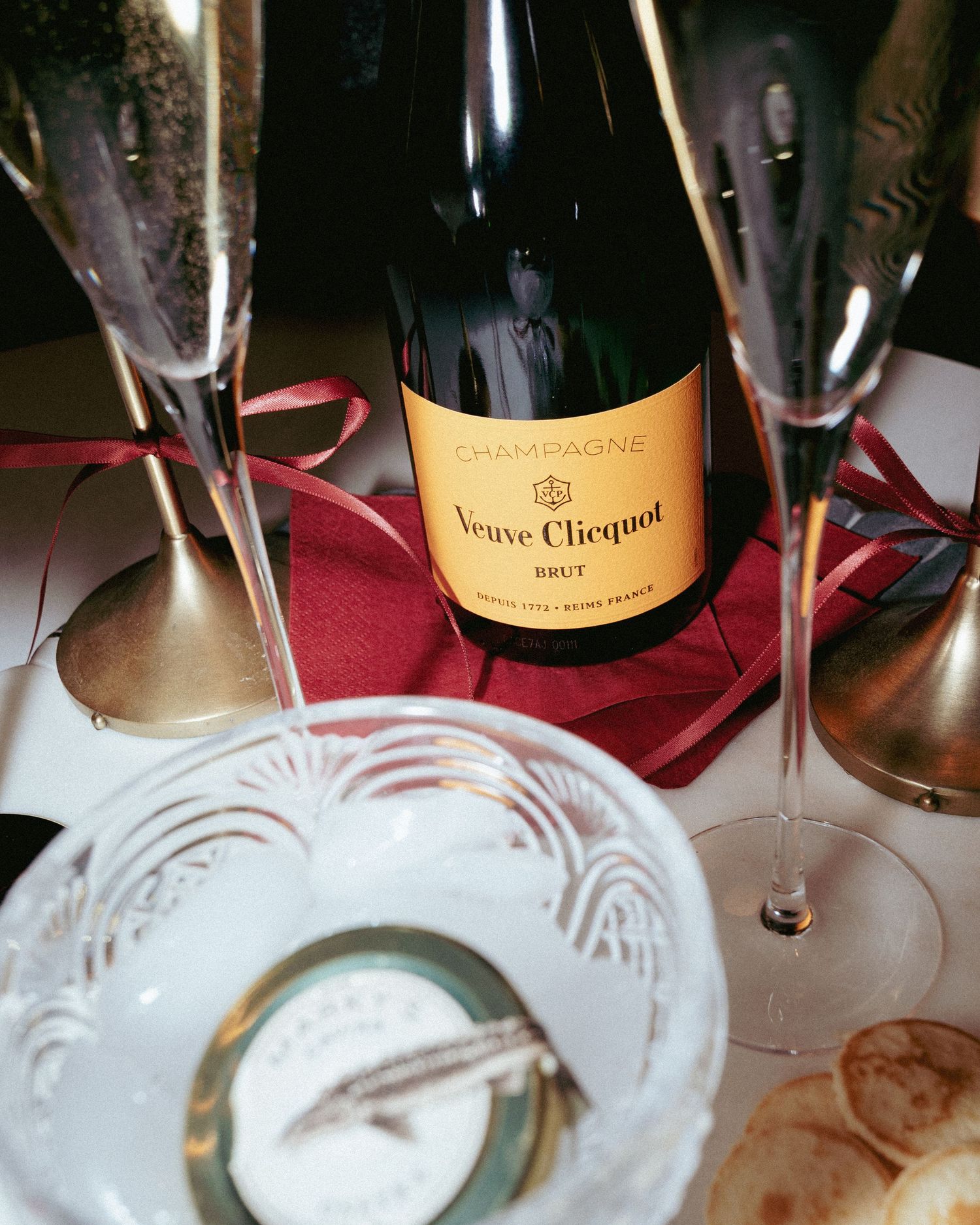 Veuve Clicquot Brut Champagne bottle with crystal flutes and caviar on elegant table setting.