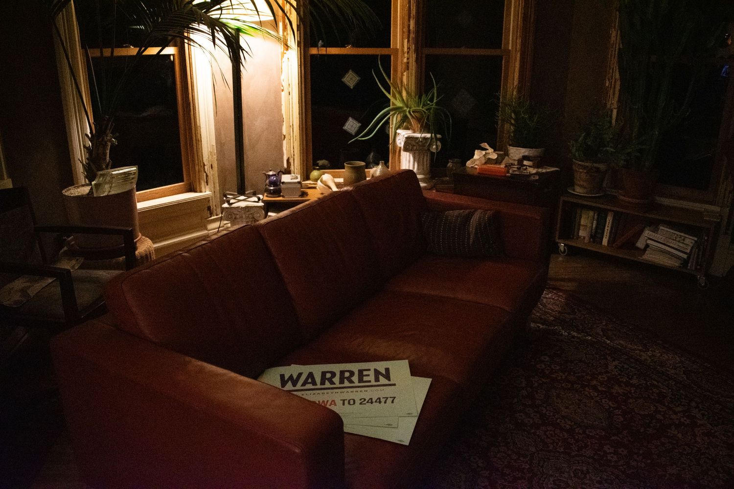 Moody evening interior with red couch and corner window illuminated by warm lamp light.