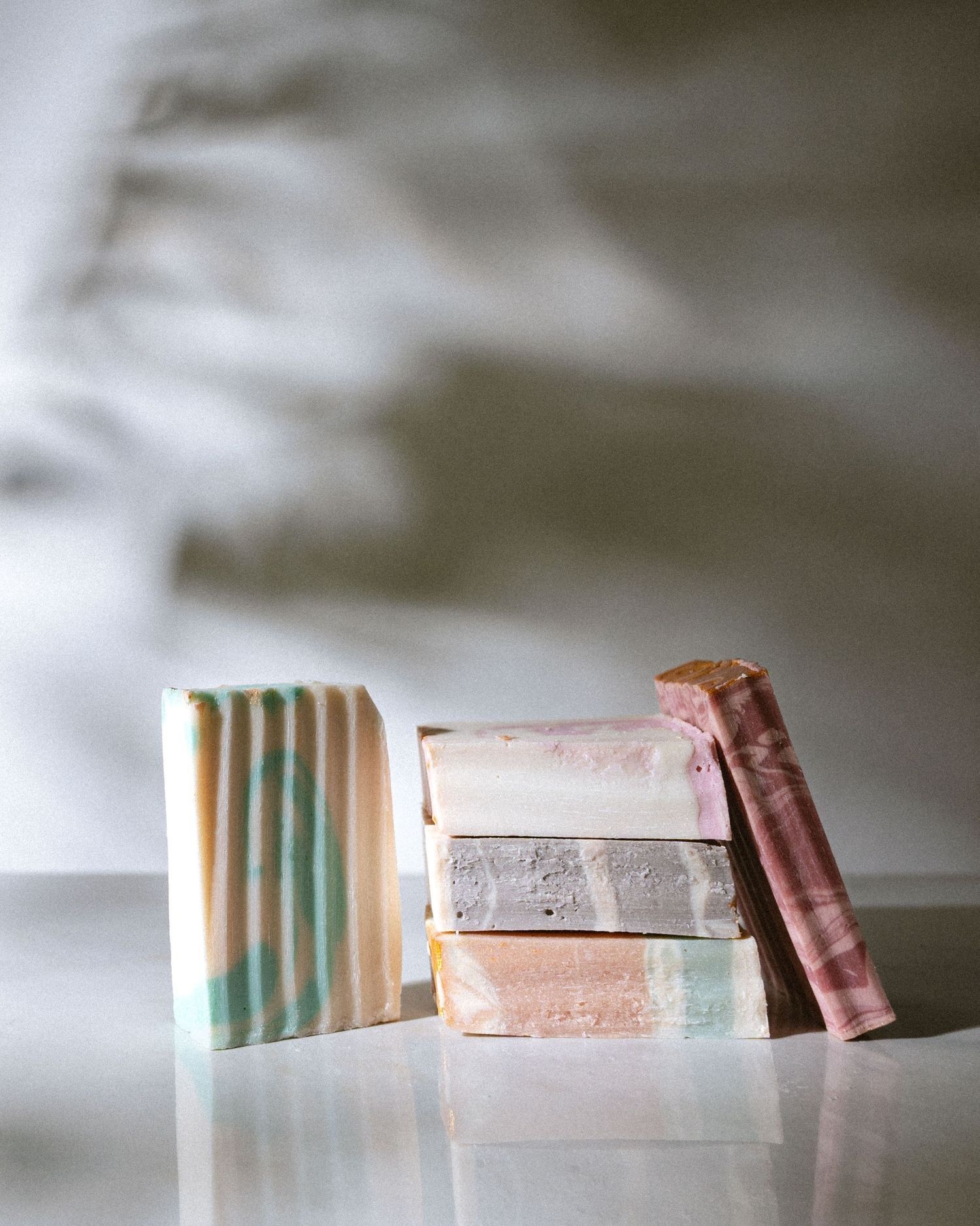A sequence of soap bars in various shades of pink and white arranged in a minimalist composition on a light surface.