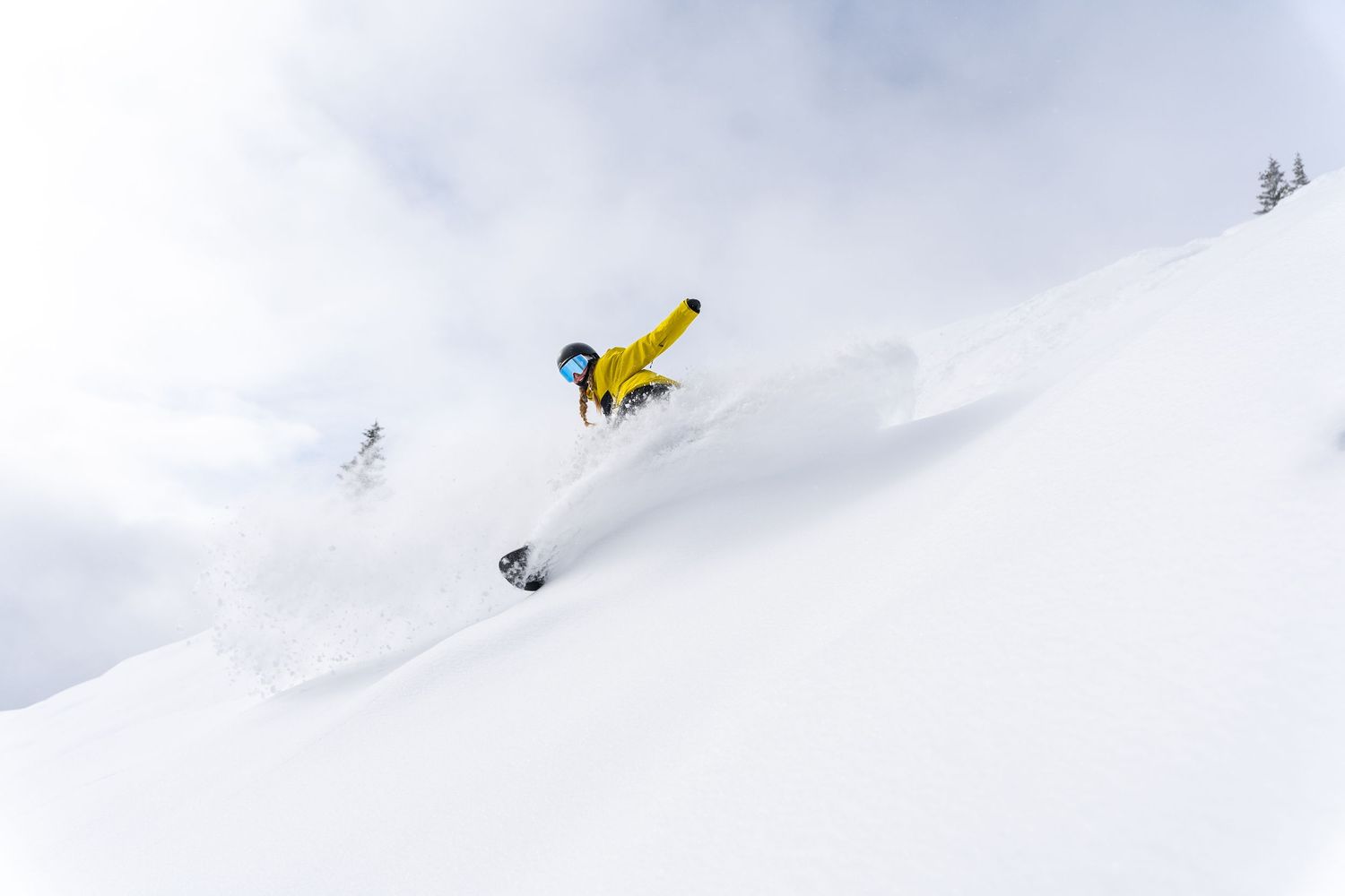 Snowboarder in yellow jacket performing aerial trick in deep powder snow.
