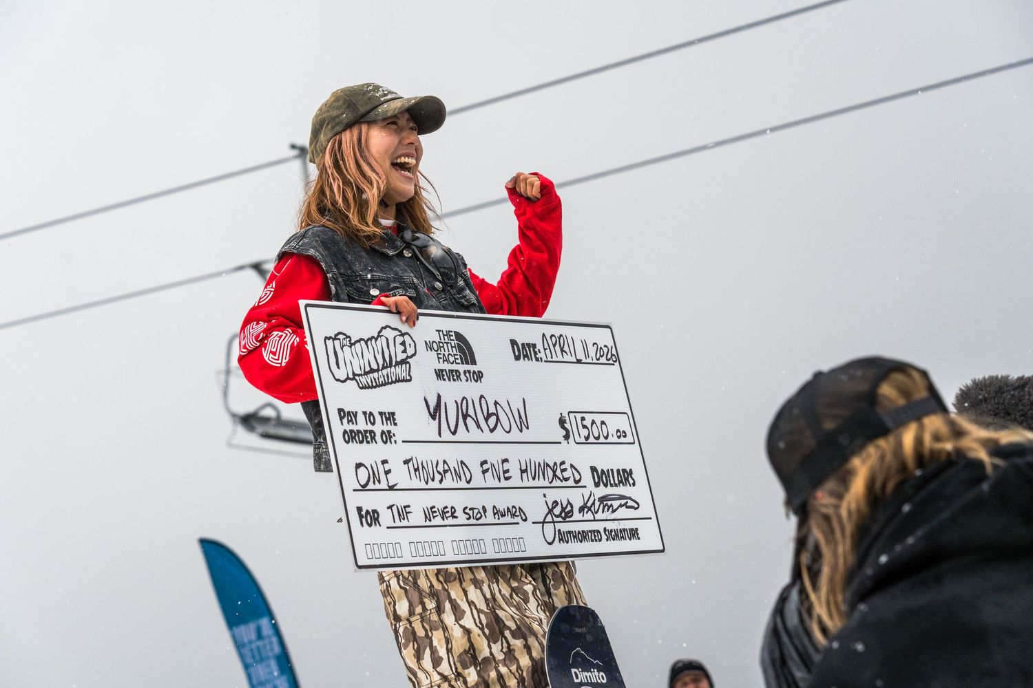 Excited snowboarder holds large prize check for $1500 at The North Face winter sports competition.