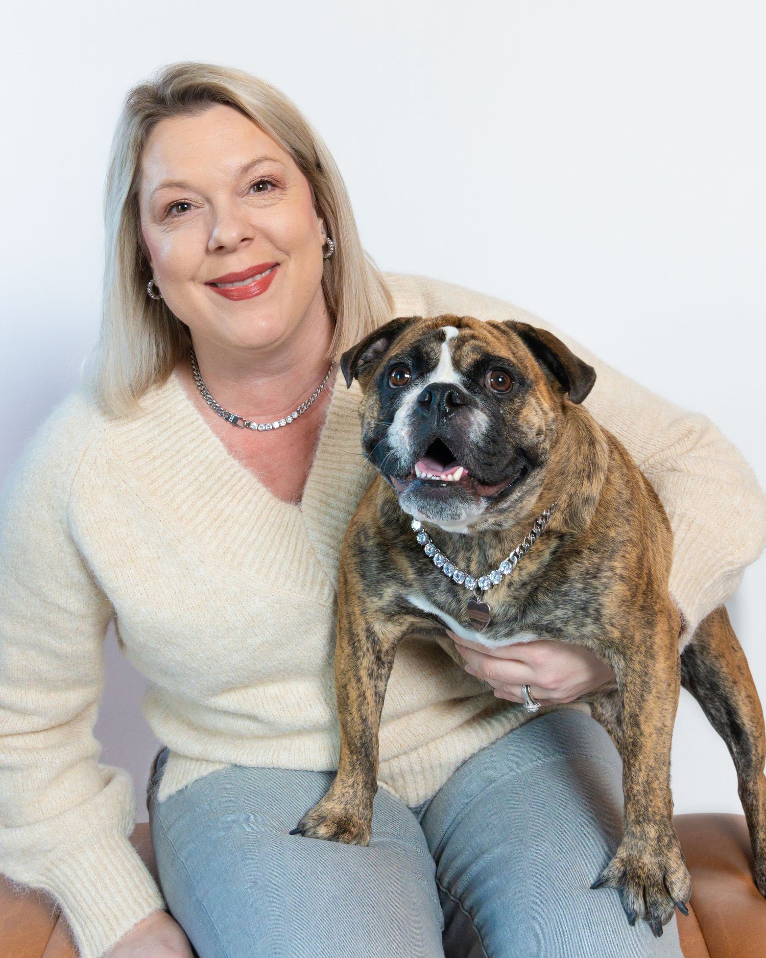 A person in a cream sweater poses with a  dog against a white background in a photo series.