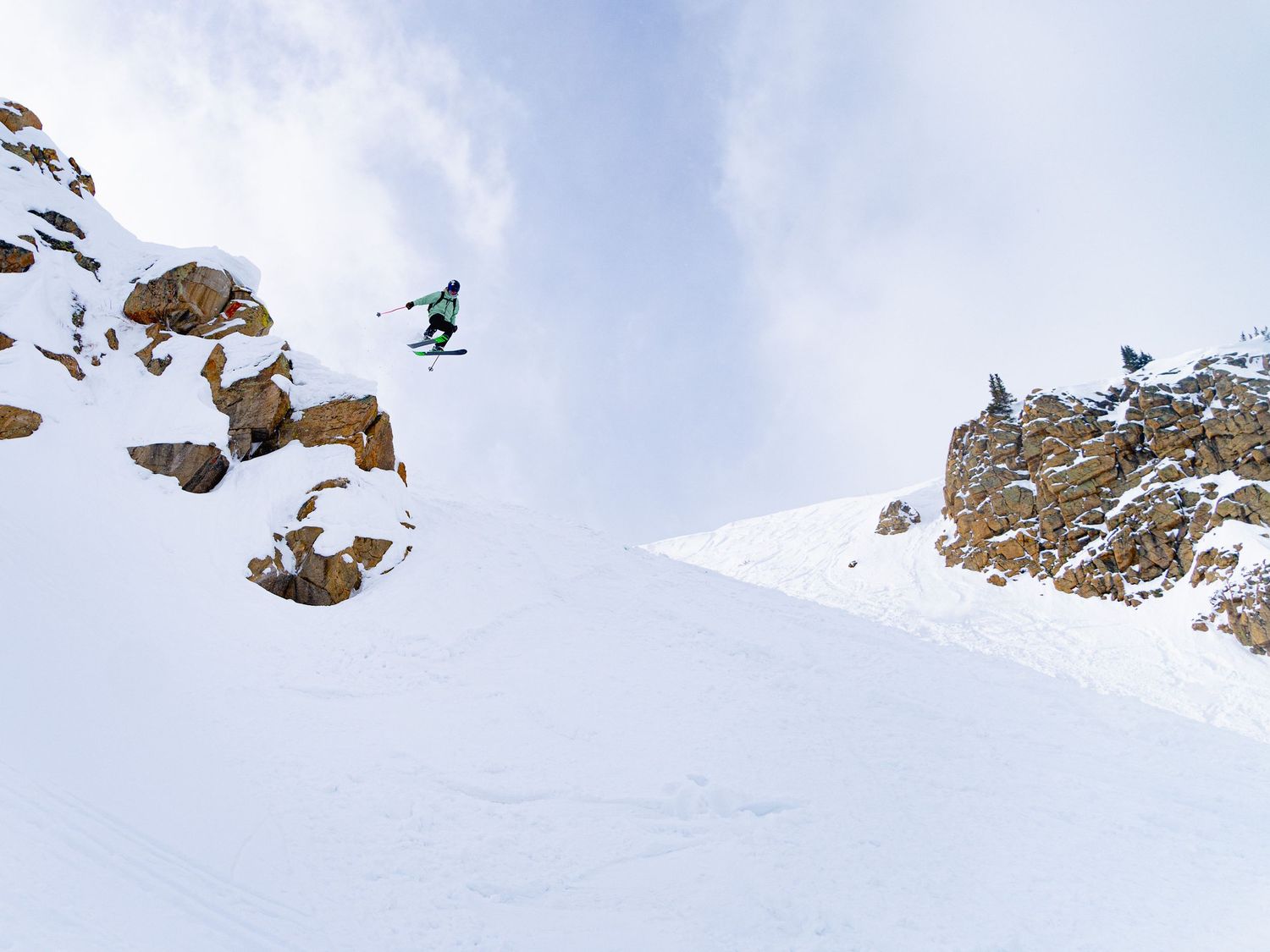 Snowboarder performing a big air jump over rocky cliffs in winter landscape.
