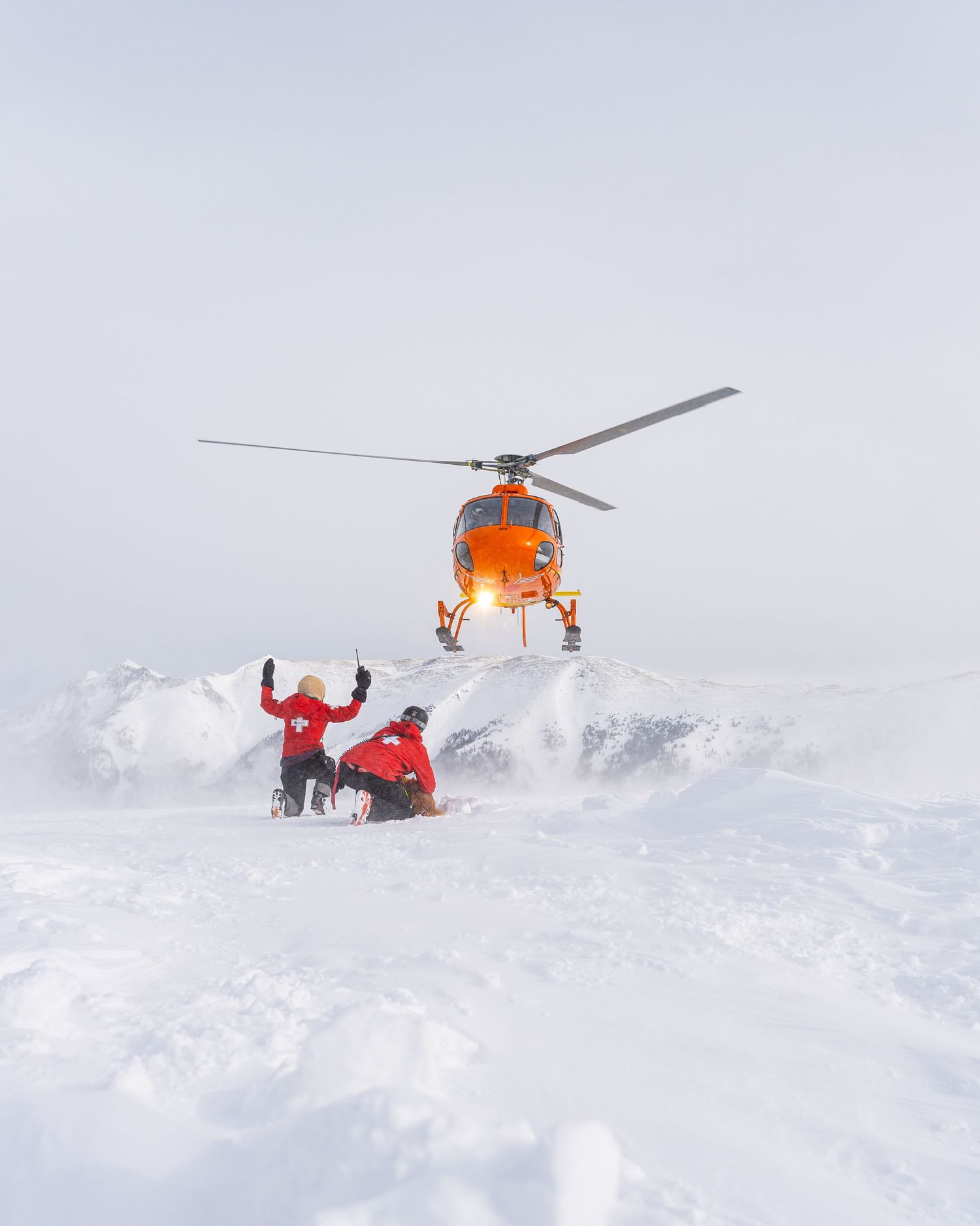 Rescue helicopter hovering over a person in red winter gear in deep snow.