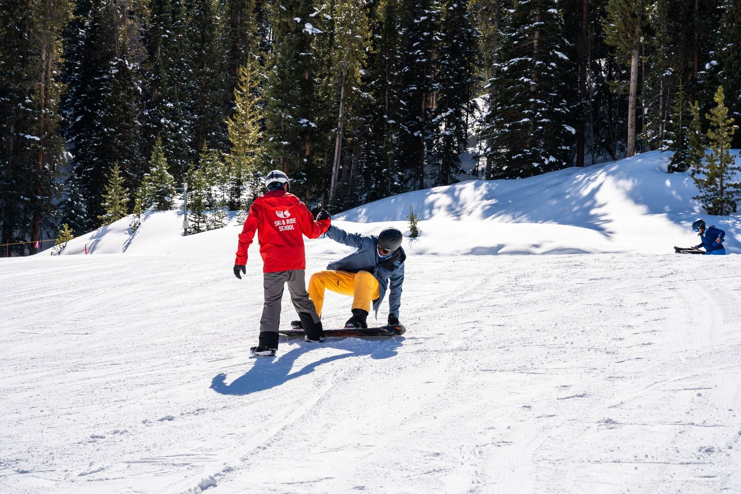 Snowboarding instruction taking place on gentle snowy slope with bright winter sunshine.