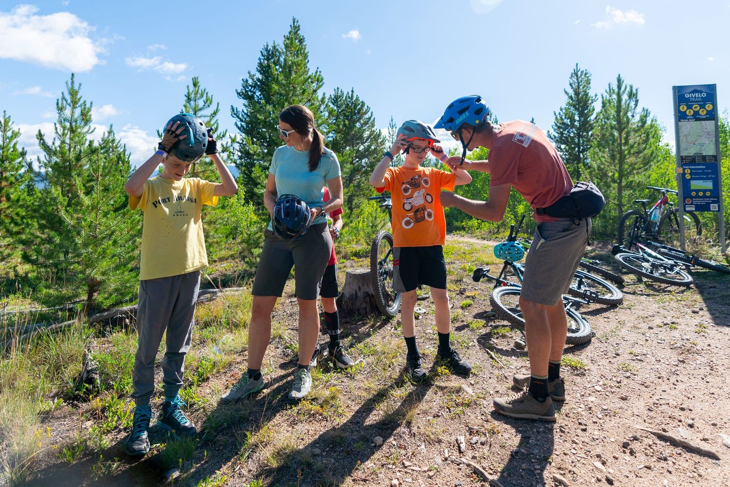 Group of cyclists taking a break on a mountain trail while checking their gear and hydrating.