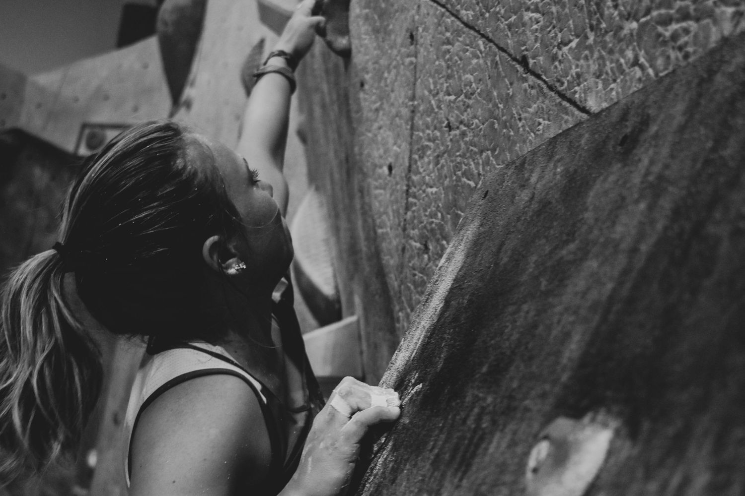 Rock climber grips onto indoor climbing wall holds in black and white monochrome.