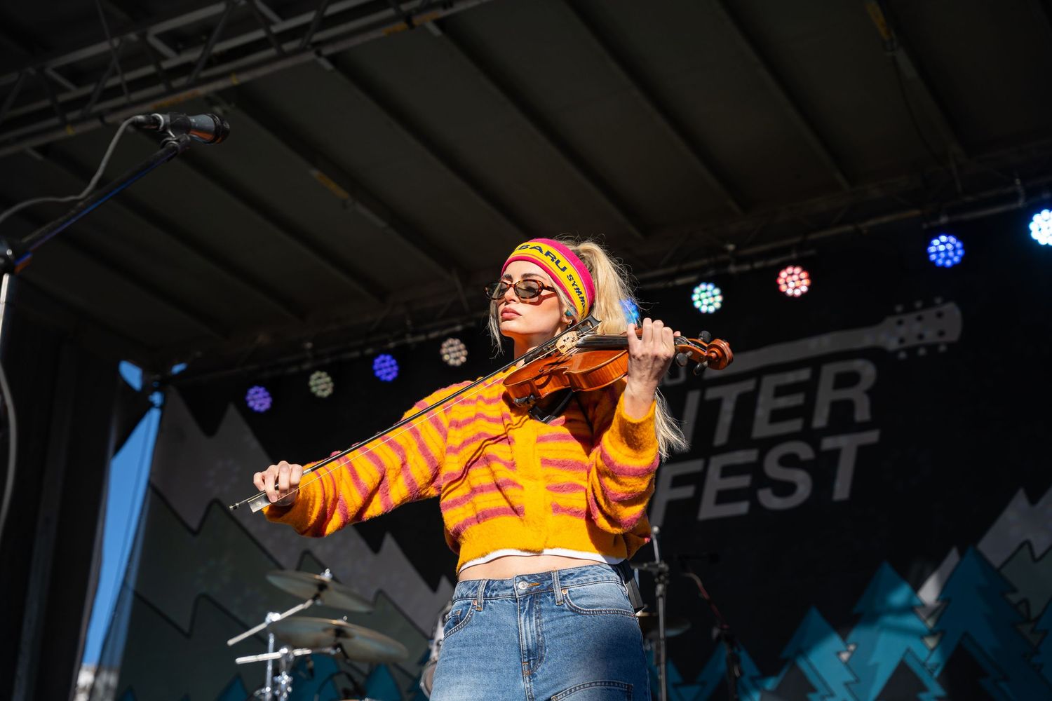 Performer in bright orange outfit on outdoor stage at winter festival.