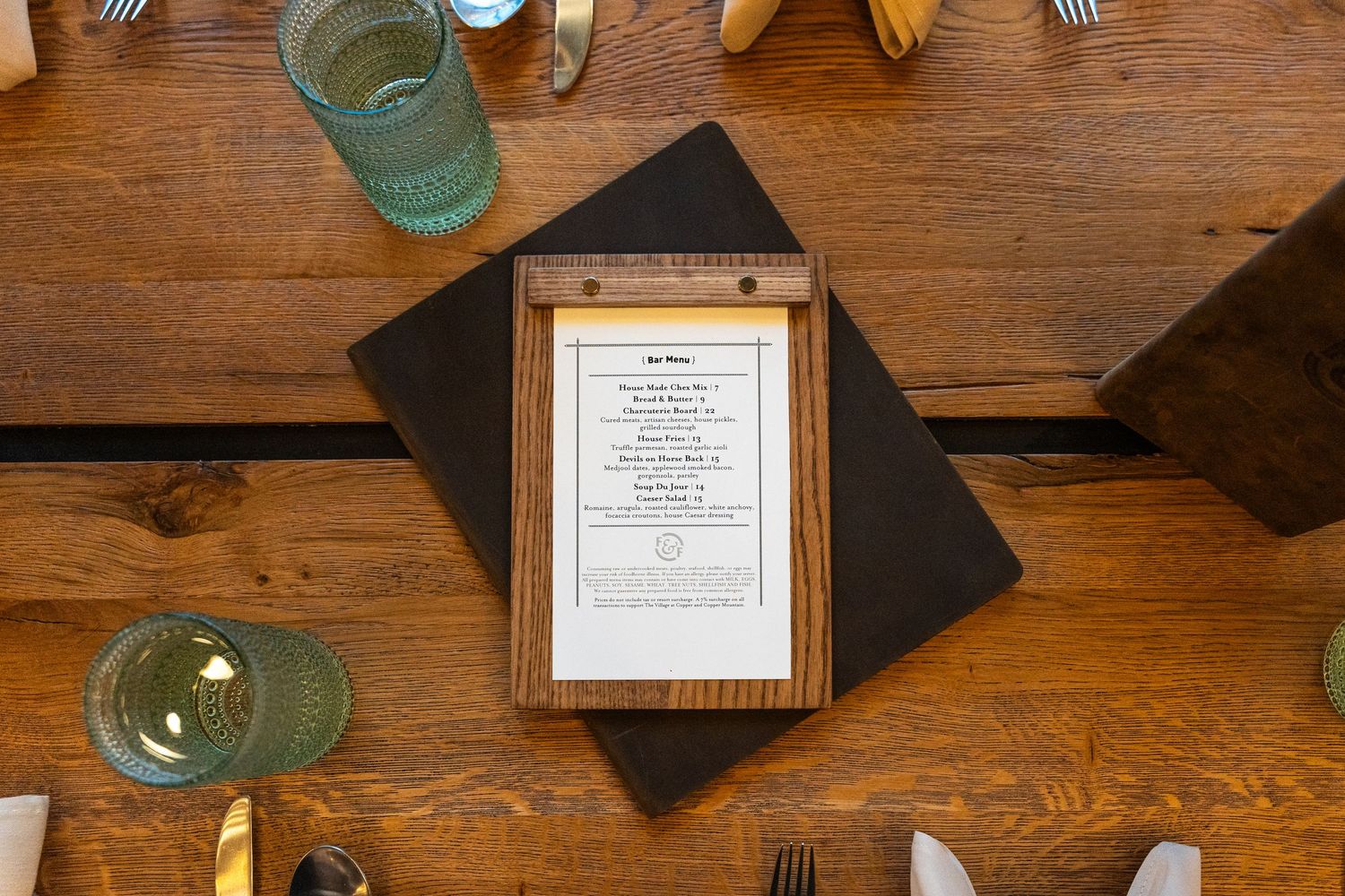 Restaurant menu and table settings on rustic wooden surface with turquoise drinking glass.