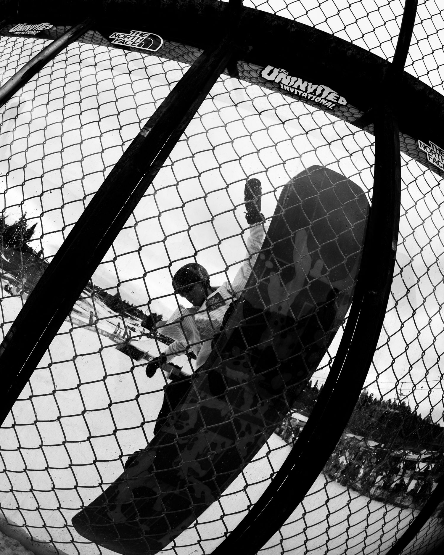 Black and white fisheye photo of a snowboarder performing a trick in a halfpipe.